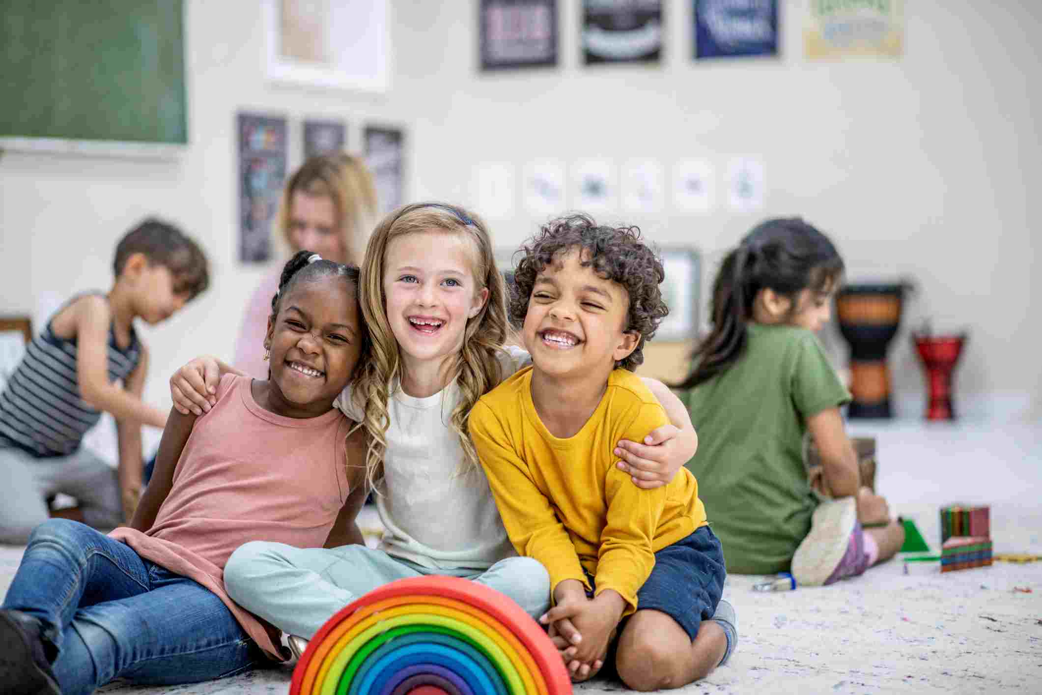 Smiling children sitting together on a rug in front of a rainbow stacking toy