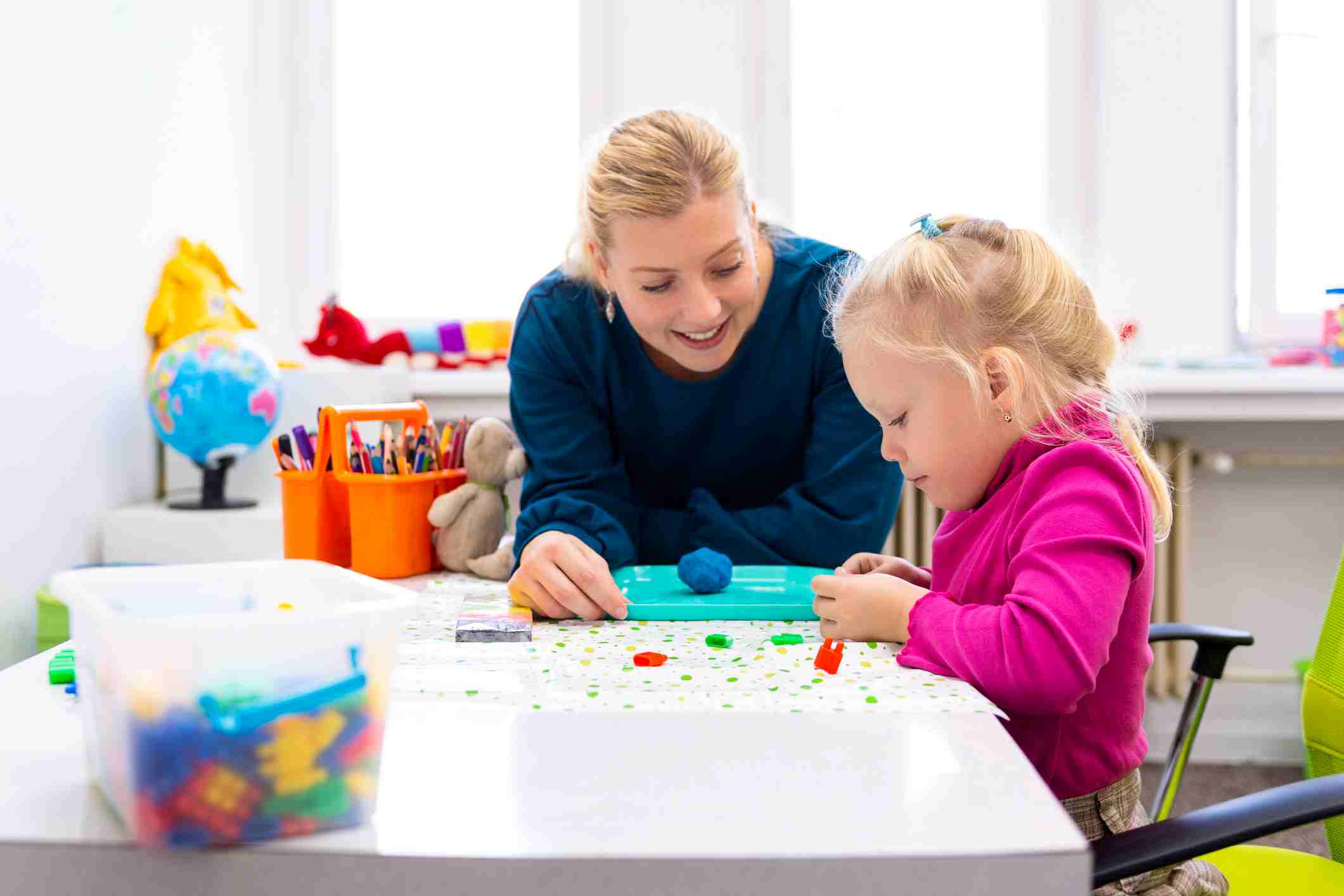 A therapist and a young girl playing with modeling clay at a table