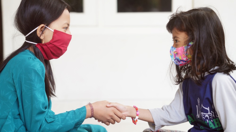 Two children wearing face masks shaking hands