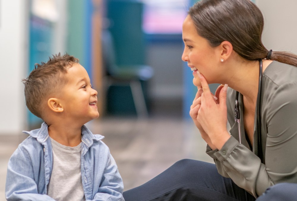 A speech-language pathologist and a young boy smiling at each other as she touches her chin