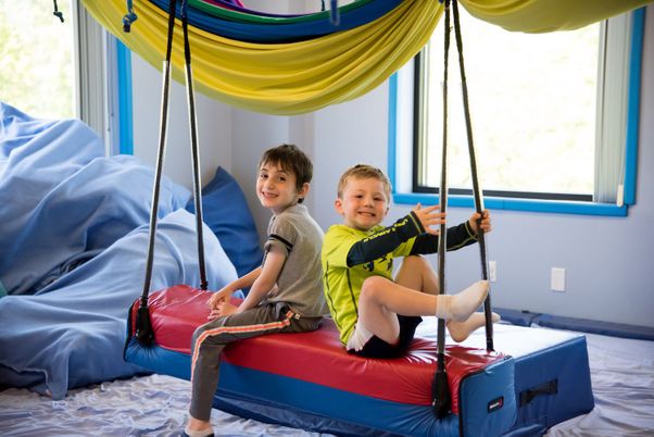 Two children balancing on a platform swing during sensory integration therapy