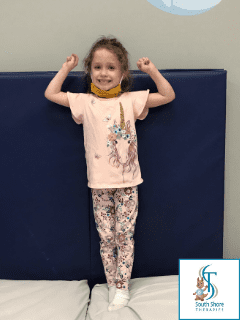 A young girl standing with her arms raised in a strong pose in front of a blue mat